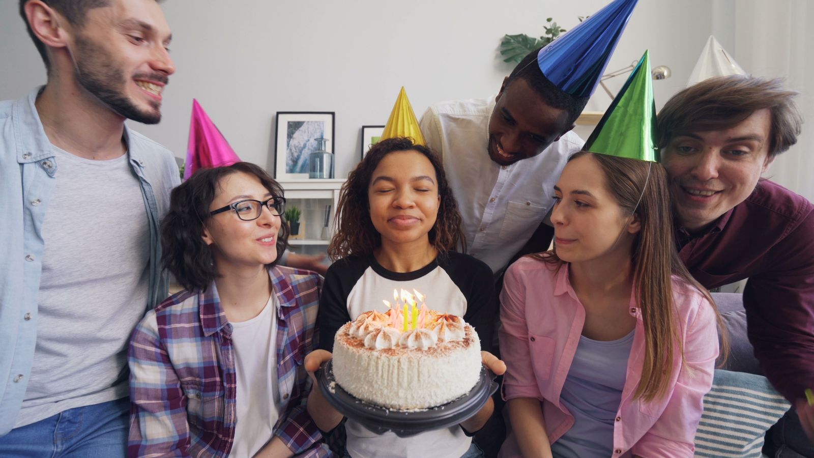 Friends in party hats around a birthday cake with candles