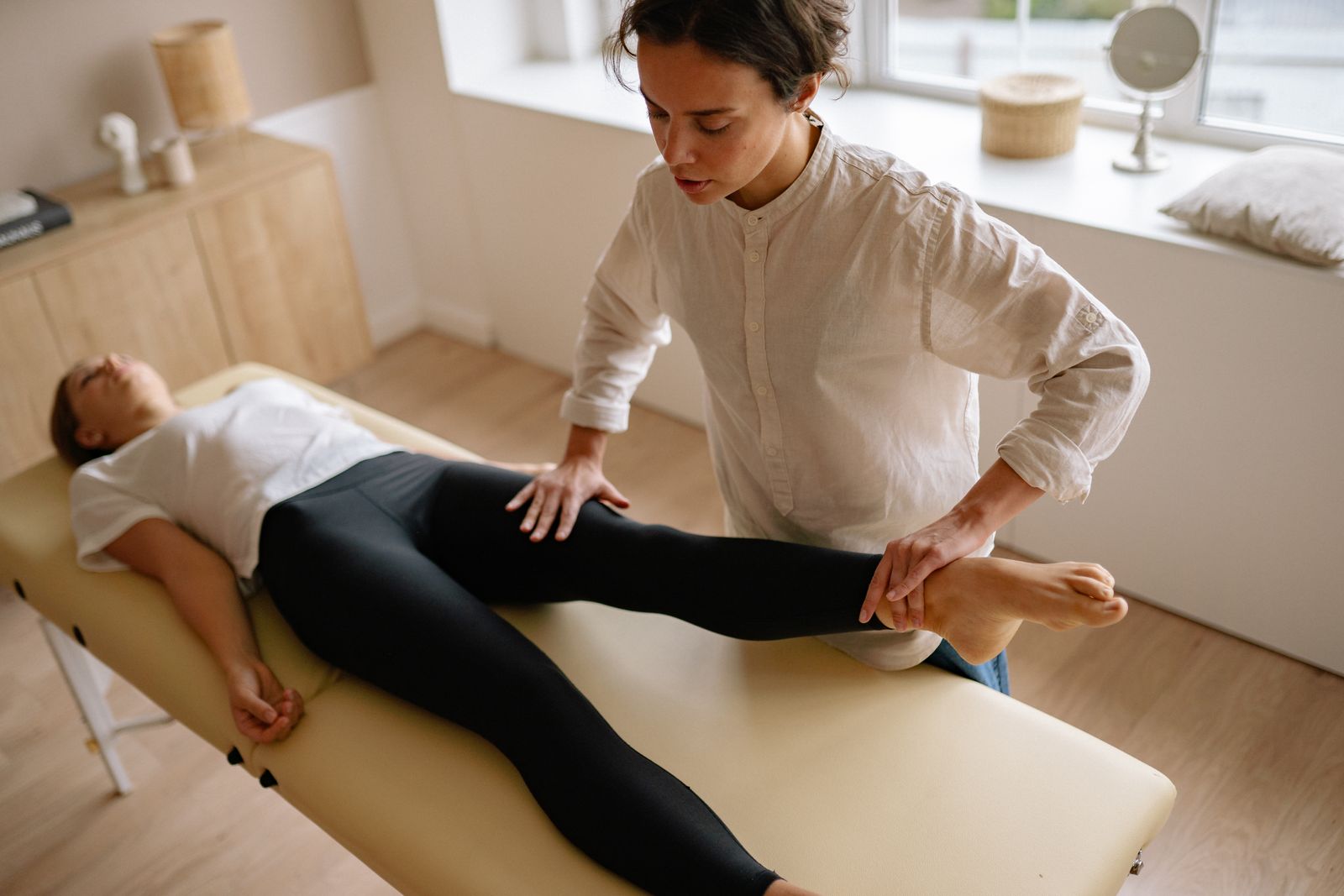Physiotherapist helping a patient with a leg exercise in a calm treatment room