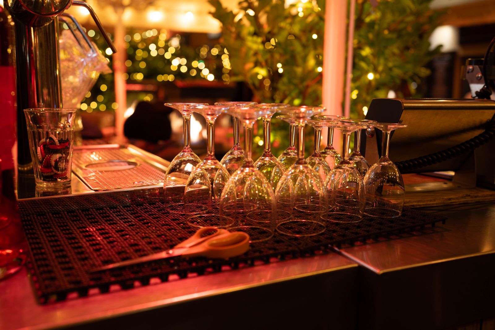 Clean wine glasses upside down on a bar mat, with warm lights behind the counter