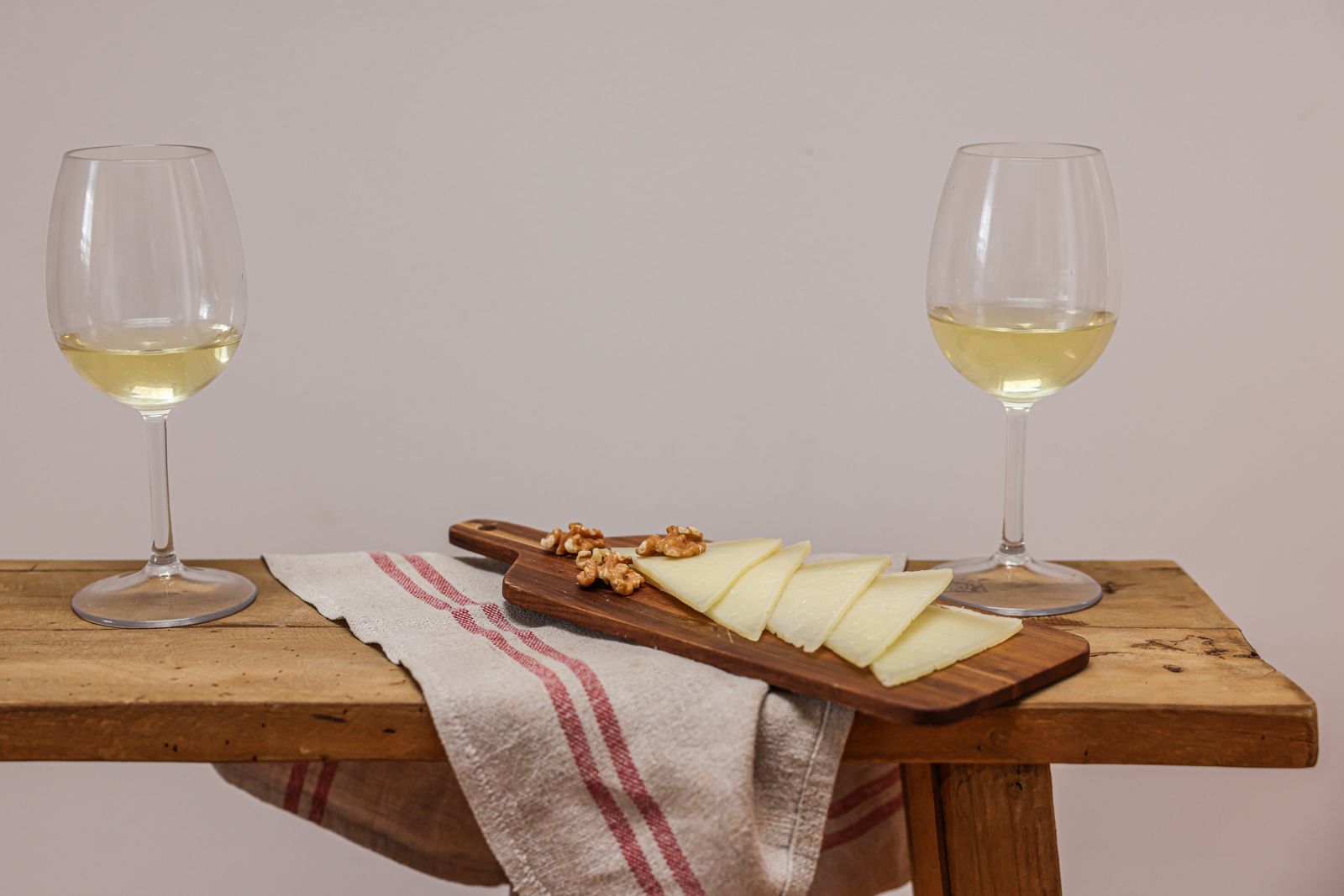 Two glasses of white wine with cheese and walnuts on a wooden board