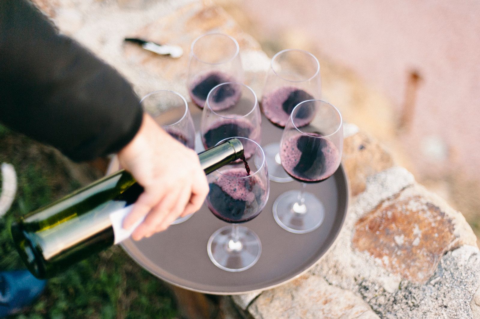 A hand pouring red wine into glasses on a round tray