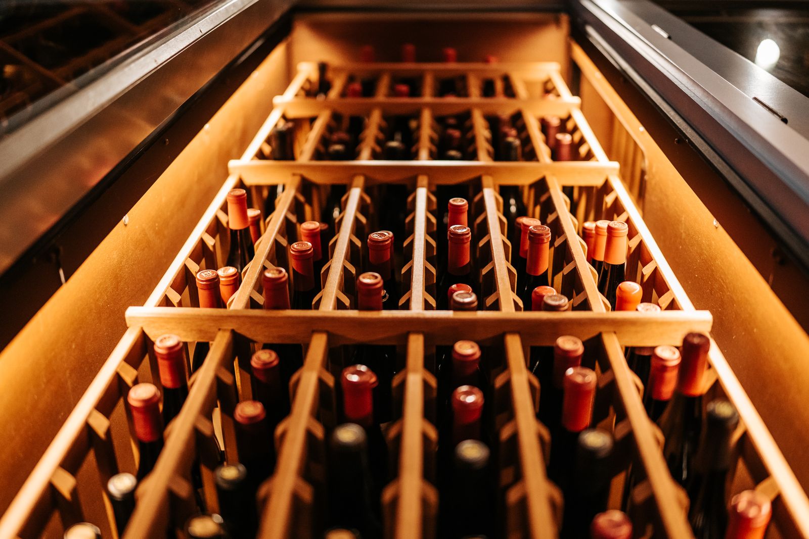 Bottles resting in a wooden wine rack, lit warmly