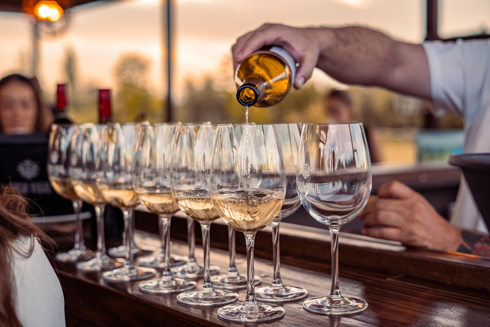 White wine poured into glasses on a wooden counter at sunset