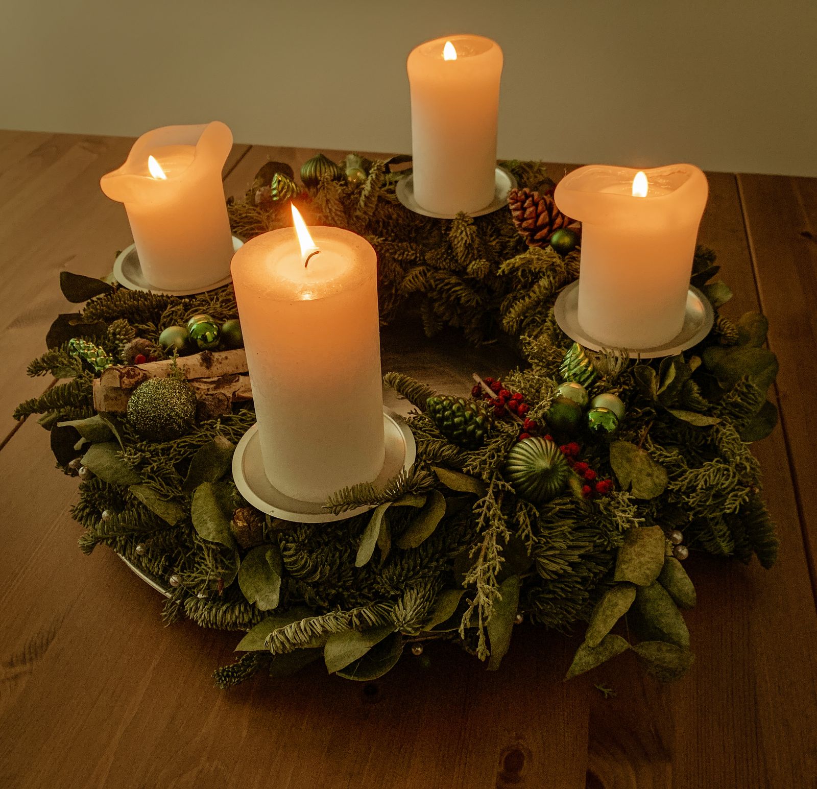 Four white pillar candles burning on a green advent wreath, seen from above