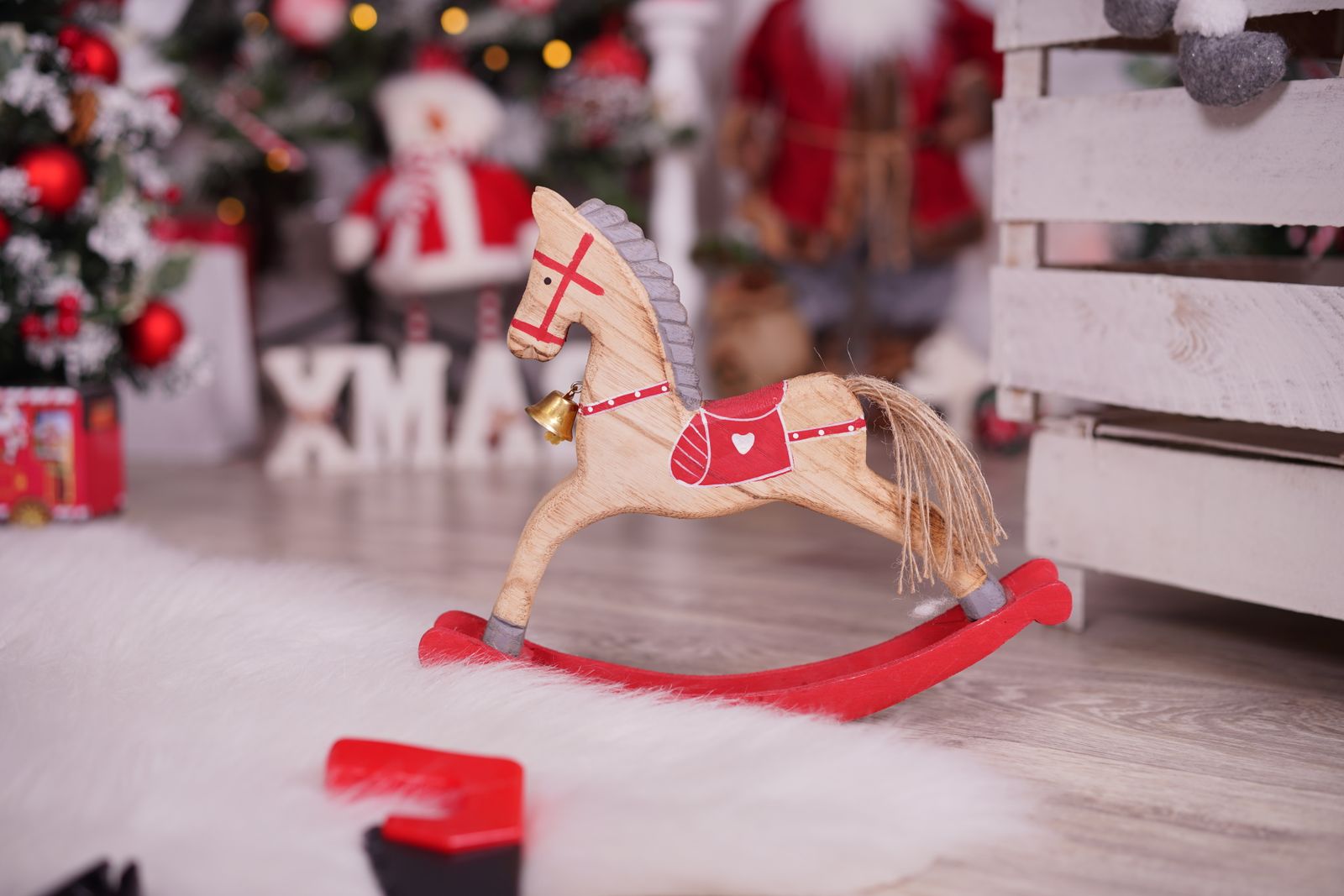 A wooden rocking horse with a red base beside Christmas decorations